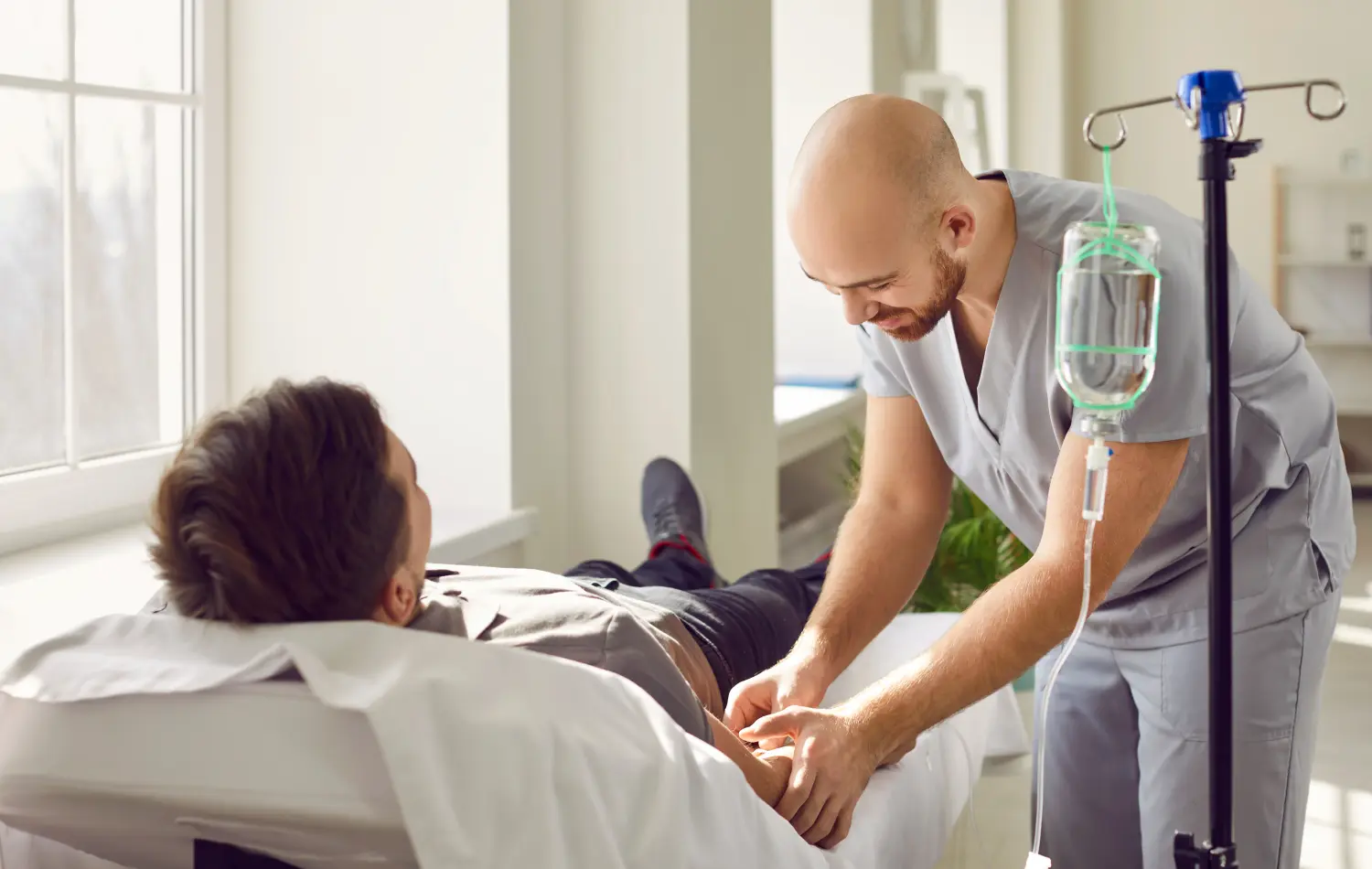 Das Pflegepersonal führt die Nadel einer venösen Infusionsleitung in die Armvene eines erwachsenen Mannes ein, der in der medizinischen Behandlung auf dem Bett liegt